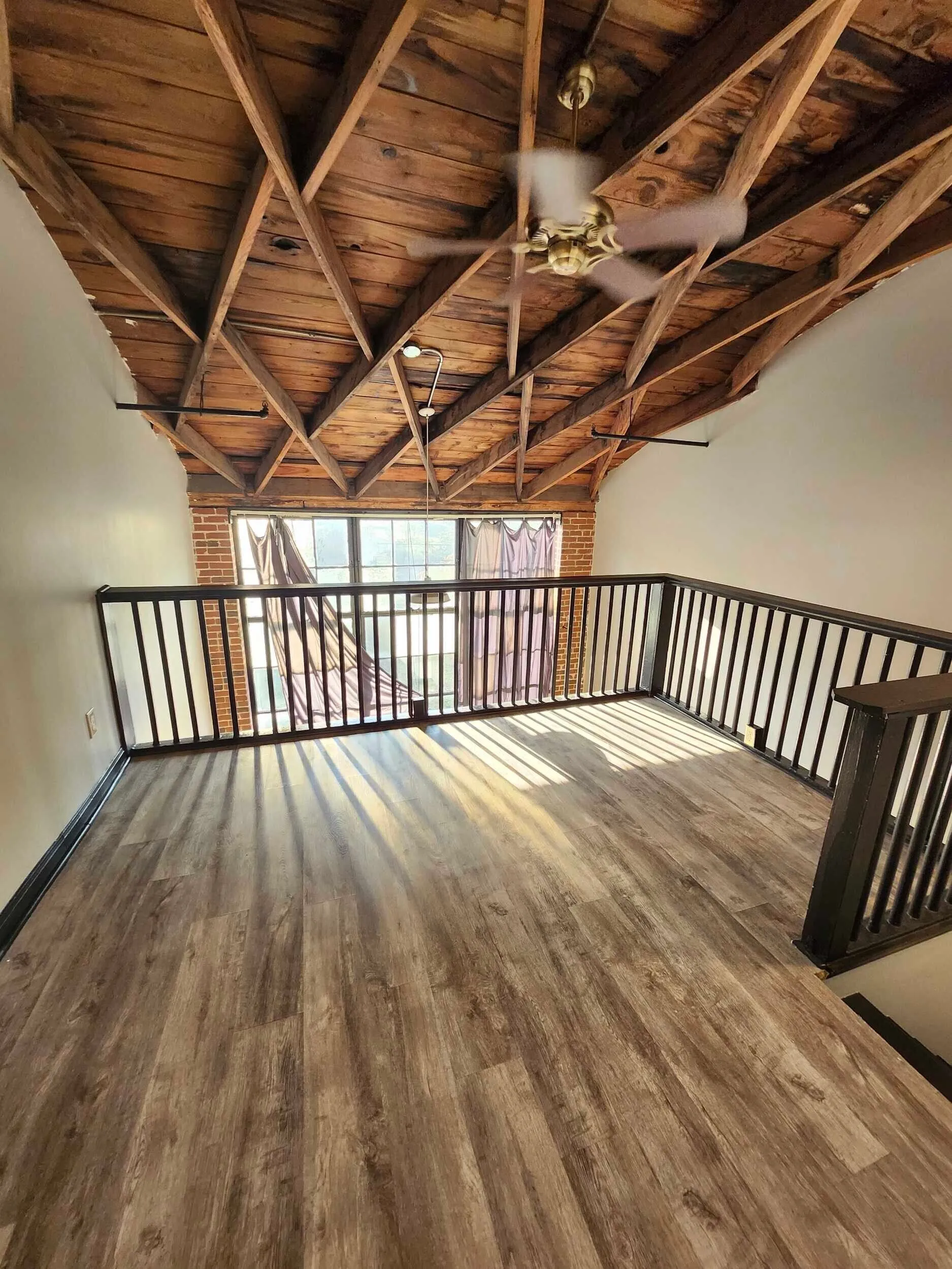 Open interior area with wood flooring, exposed rafters, and a window wall